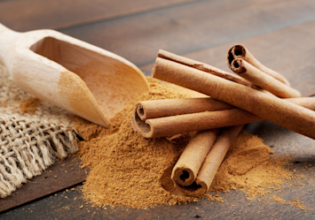 Cinnamon sticks and ground cinnamon powder on a wooden surface, illustrating ingredients that dog owners may wonder about feeding to their pets, addressing the question "Can dogs eat cinnamon?" and the safety of cinnamon for dogs.